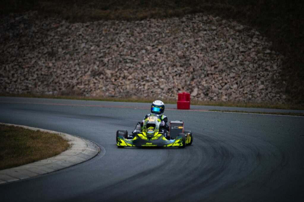 Kartfahrer in neongrün-schwarzem Kart auf Strecke von vorn