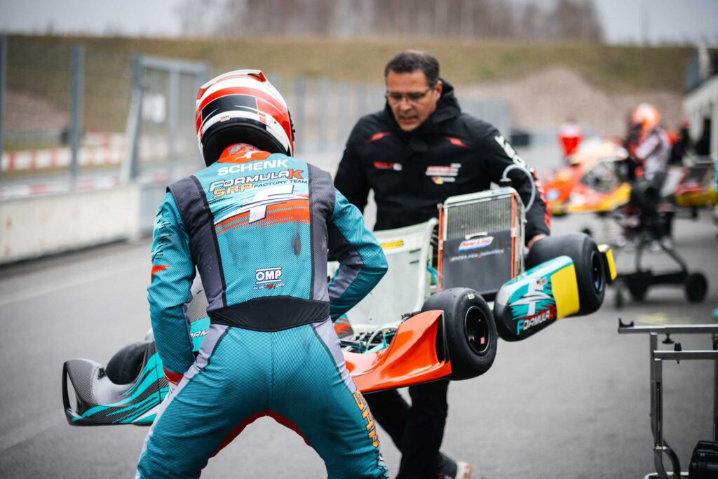 Ein Fahrer in seiner Sportkleidung von hinten fotografiert, hebt mit einem Mechaniker das Kart vom Bock