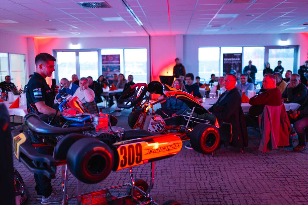 Aufgebocktes Kart, an dem Nils Tröger erklärt, im Hintergrund Zuschauer