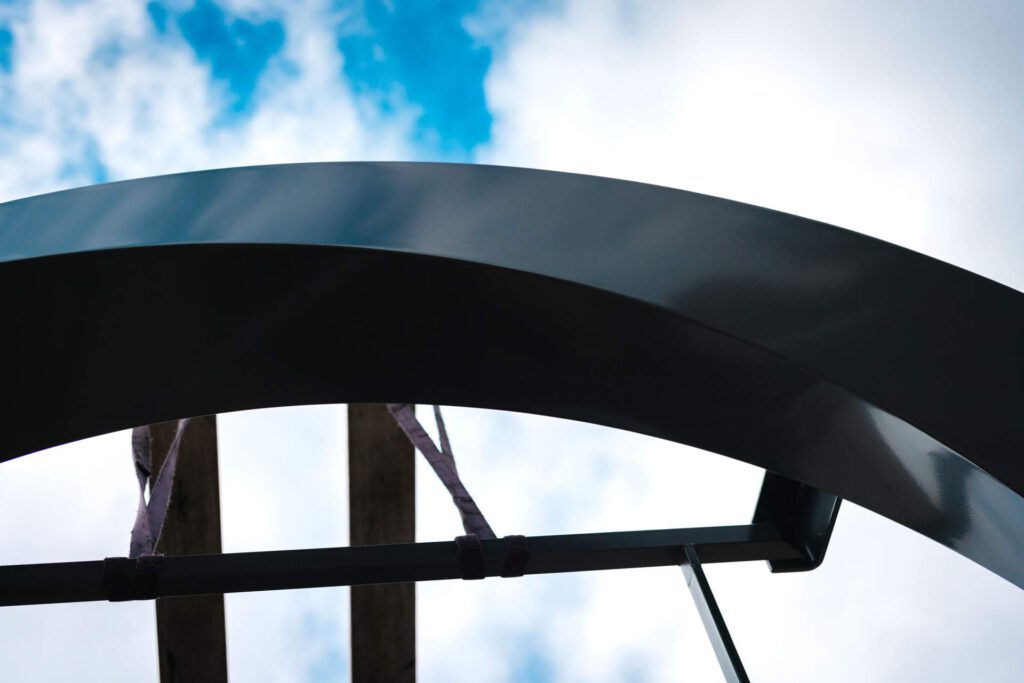 Von unten fotografierte Nahaufnahme des dunklen Logos, darin spiegeln sich die Wolken am Himmel