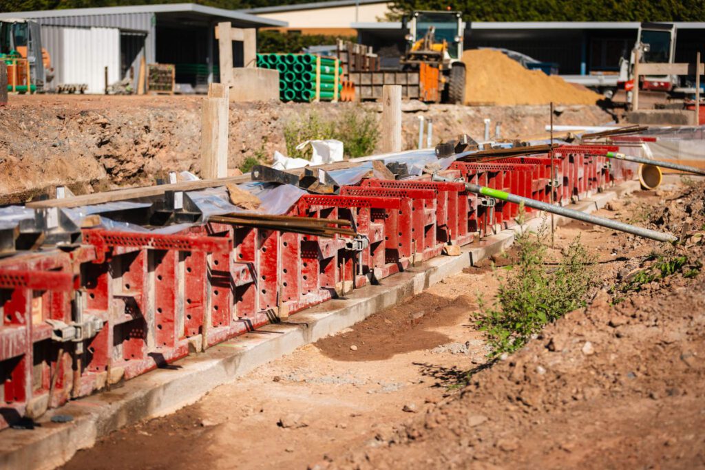 Eine Nahaufnahme auf Bodenebene von roter Kunststoffschalung, die zum Gießen einer Betonfundamentwand auf einer Baustelle verwendet wird.