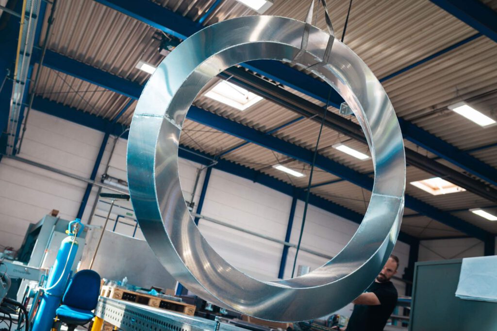 Ein großes, glänzendes Metallobjekt in Form eines Ringes hängt an einem Kran in einer Produktionshalle und wartet auf die weitere Bearbeitung.