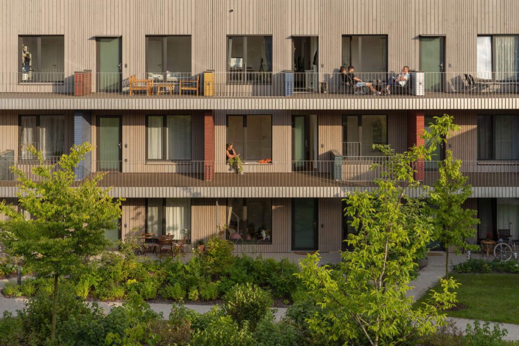 Balkonbänder der Holzfassade: Frontalansicht der Holz-Hybrid-Fassade mit durchgehenden Edelstahlgeländern. Gut sichtbar sind die integrierten Zugstäbe und die lasergeschnittenen Einzelteile.