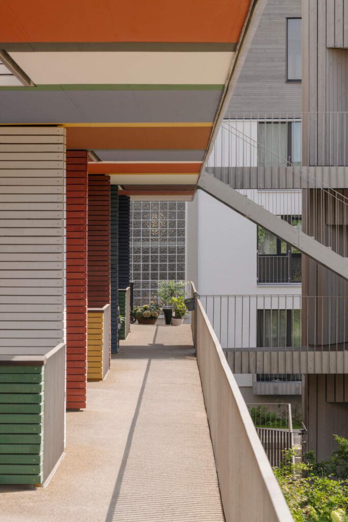 aubengang mit Farbakzenten: Ansicht eines Laubengangs mit filigranem Edelstahlgeländer. Im Hintergrund setzen farbige Wandelemente Akzente in der Holzbauweise.