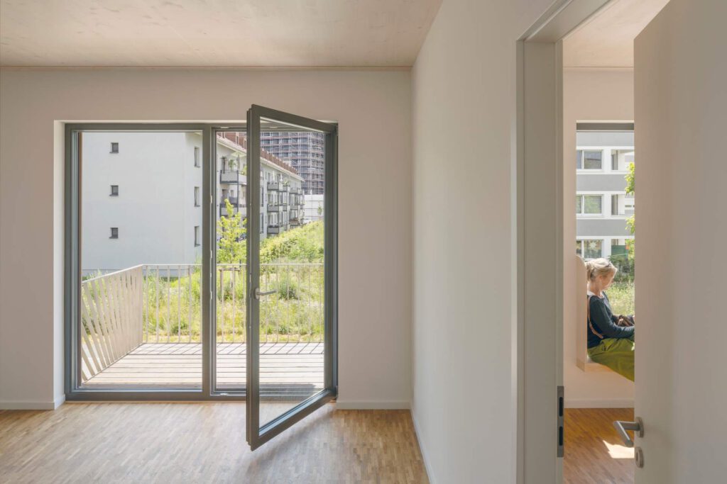 Innenansicht mit Balkonaustritt: Blick aus einer Wohnung nach draußen. Die raumhohen Fenster werden durch französische Geländer aus Edelstahl gesichert, die einen freien Blick ins Grüne ermöglichen.