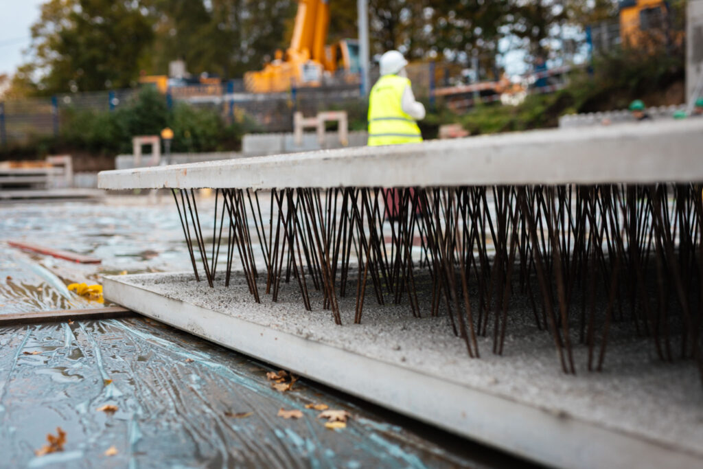 Nahaufnahme einer Betonfertigplatte, die mit herausragenden Bewehrungsstählen auf einer mit Folie abgedeckten Baufläche liegt.