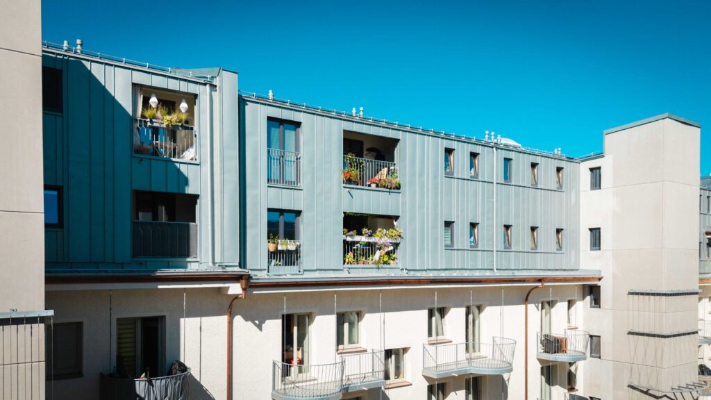 Ansicht eines Innenhofs oder einer Rückseite des Wohngebäudes mit einem Mix aus Holzverkleidung und hellen Fassaden, sowie modernen Balkonen und Loggien.