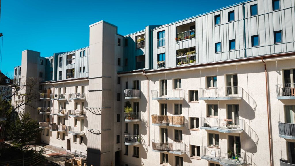 Breitere Ansicht des Innenhofs, die mehr von der Gebäudestruktur mit den zahlreichen runden Balkonen und der modernen Aufstockung zeigt.