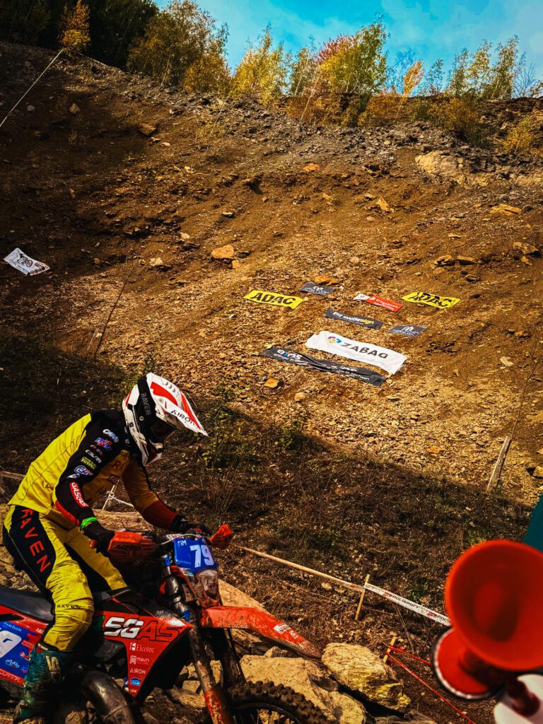 Enduro-Fahrer mit gelbem Trikot und der Startnummer 79 auf einem GasGas-Motorrad erklimmt eine steile, steinige und trockene Geröllhalde bei einem Offroad-Rennen. Im Hintergrund sind Sponsoren-Banner wie ADAC und ZABAG sichtbar.