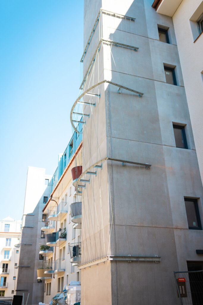 Runde Balkone mit schlichten Metallgeländern an der modernen hellen Fassade eines Wohngebäudes bei starkem Sonnenlicht.