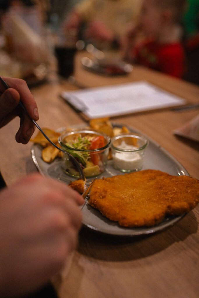 Gedeckte Tische und entspannte Atmosphäre im Restaurant A la Kart während des Abendessens. Auf dem Teller ein saftiges Schnitzel mit Pommes