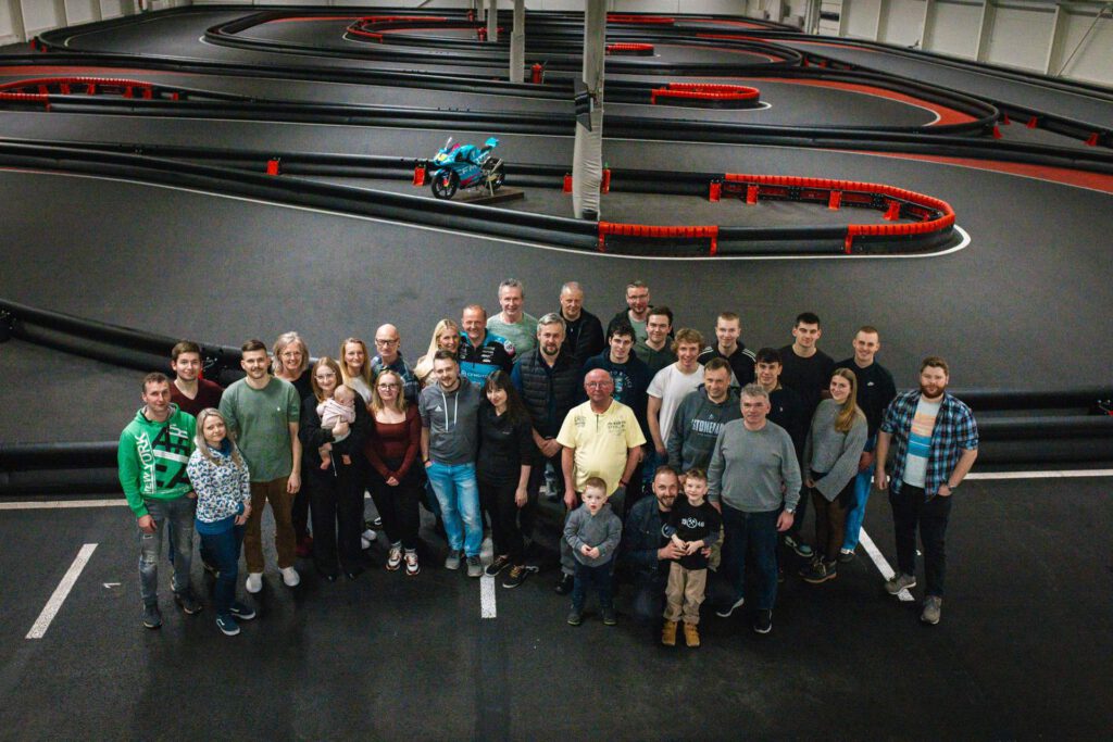 Gruppenfoto des geamten Teams auf der Indoor-Kartbahn aus der Vogelperspektive.