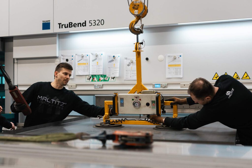 Präzisionsarbeit an der TruBend 5320: Mitarbeiter nutzen einen Vakuumheber, um schwere Blechplatten sicher für die Abkantpresse zu positionieren.