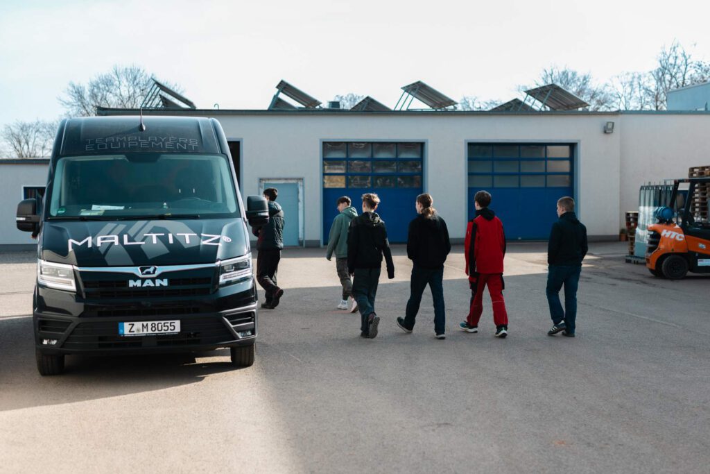 Teilnehmer der Woche der offenen Unternehmen auf dem Betriebsgelände der Firma Maltitz, flankiert von einem schwarzen MAN Service-Transporter.