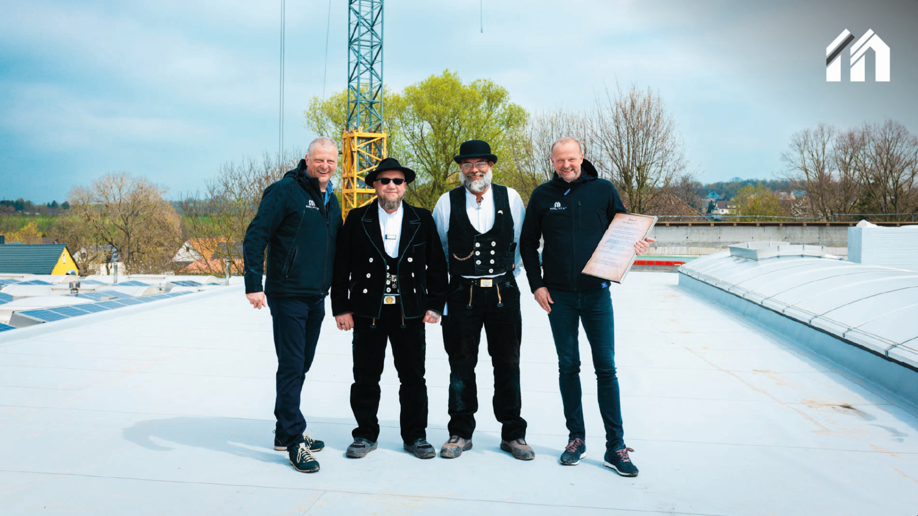 Gruppenbild auf dem Hallendach: Geschäftsführer und Zimmerleute in traditioneller Kluft mit der Firstrede.