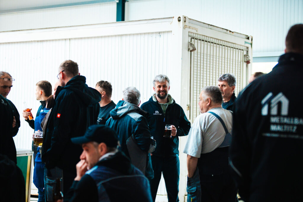 Geselliges Beisammensein: Mitarbeiter unterhalten sich bei Getränken vor einem Container in der Werkhalle.