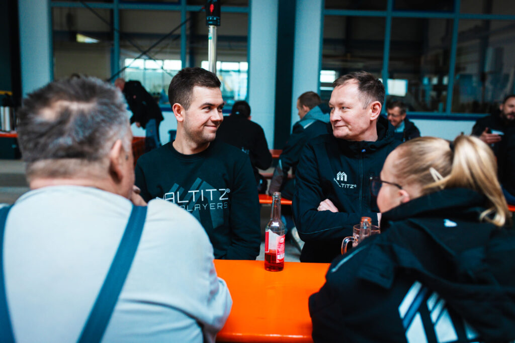 Team-Moment: Zwei Mitarbeiter in Firmenkleidung sitzen lachend an einem Biertisch während der Richtfest-Feier.