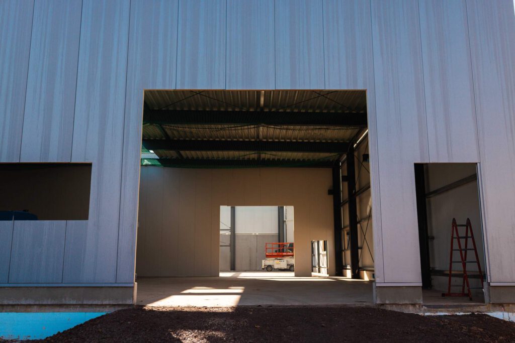 Innenansicht der neuen Industriehalle mit bereits montierten Sandwichpaneelen und Lichtblick durch die Toröffnungen.