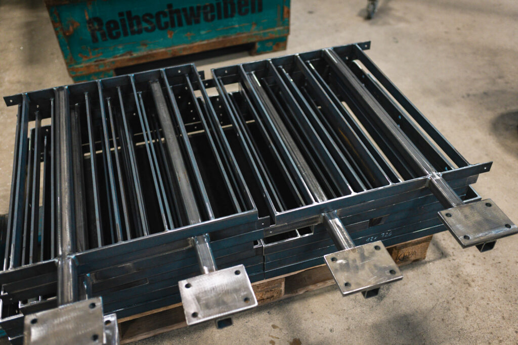 Stapel von präzise gefertigten schwarzen Metallgeländer-Elementen mit Montageplatten für die Bavarian International School.