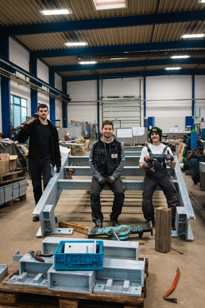 Drei stolze Metallbauer posieren in der Werkstatt vor der massiven Stahlkonstruktion einer Fluchttreppe für das Schulgebäude.