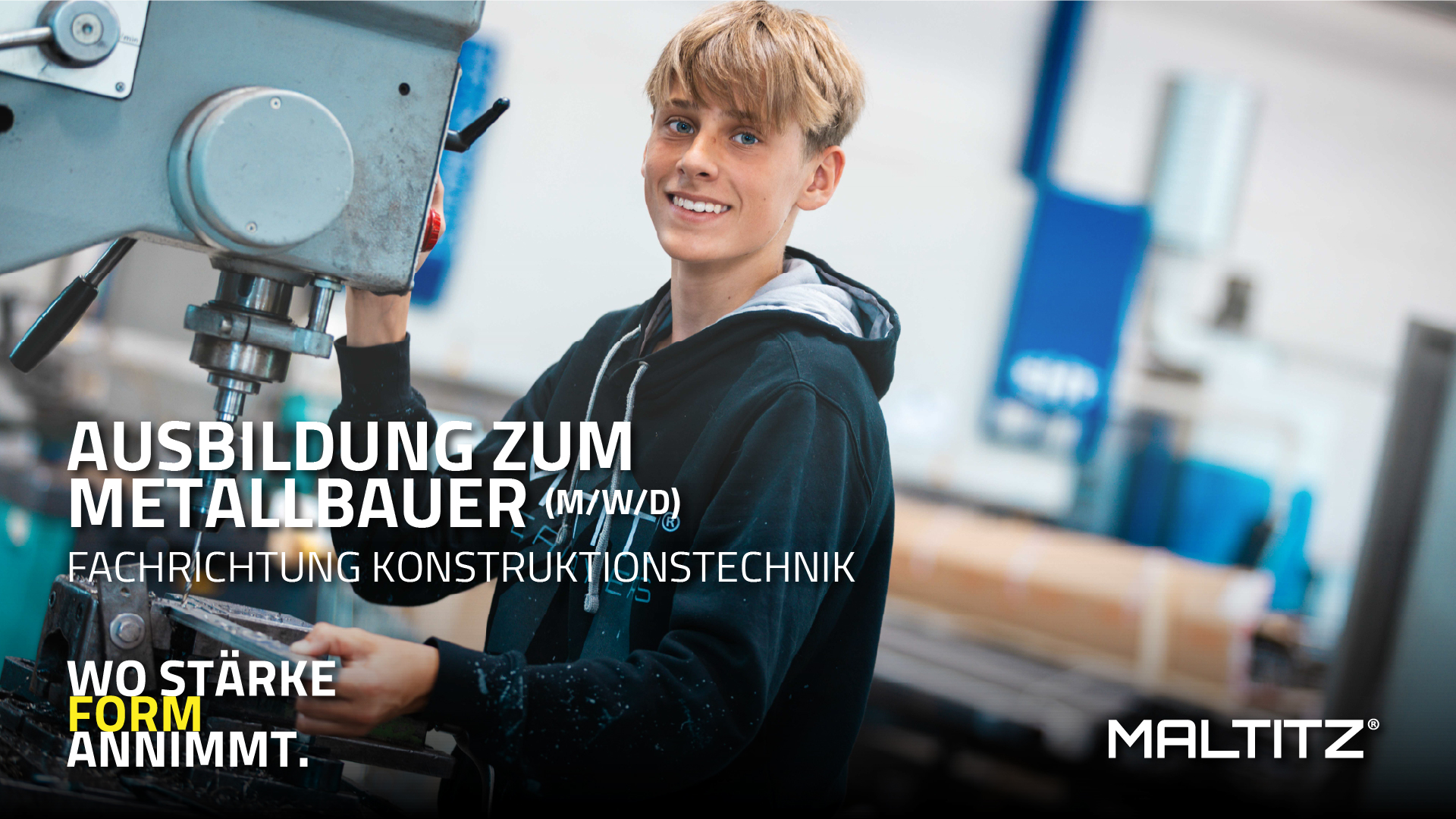 Ein Werbebanner für eine Berufsausbildung. Im Zentrum steht ein lächelnder junger Mann in einem schwarzen Kapuzenpullover, der in einer Werkstatt an einer großen Metallbohrmaschine arbeitet. Er schaut direkt in die Kamera. Der Hintergrund ist leicht unscharf und zeigt eine industrielle Fertigungsumgebung.