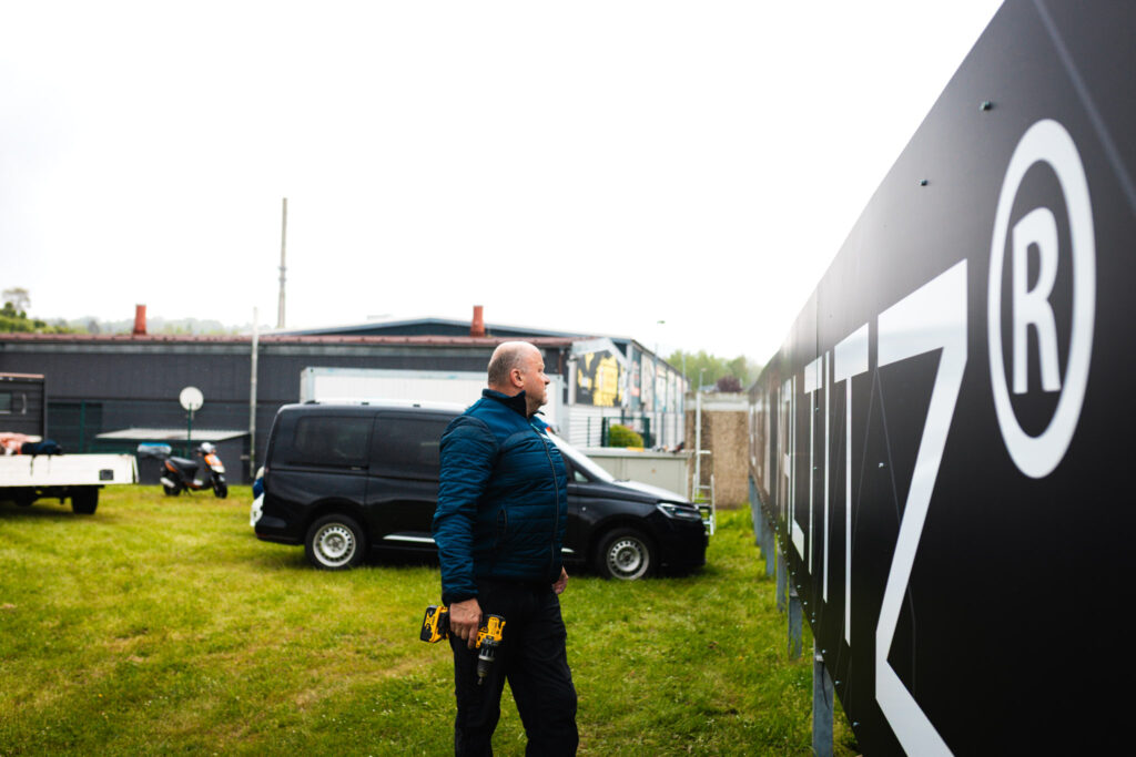 Montage der Maltitz Werbetafel für die MotoGP am Sachsenring durch ein Handwerker-Team im Außenbereich.