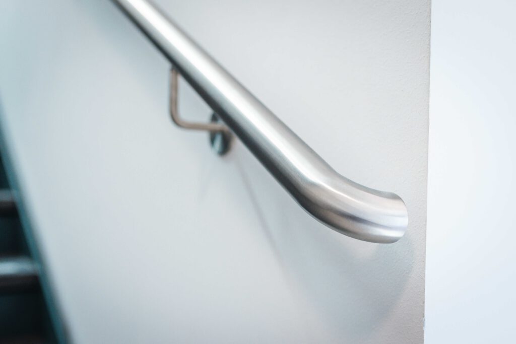 Detailaufnahme eines hochwertigen Edelstahl-Handlaufs in runder Form, stabil an einer weißen Wand montiert – Metallbau-Handwerk in Perfektion.