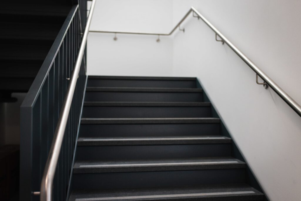 Volle Ansicht der neuen Metalltreppe im THW Dresden mit dunklen Stufen, kontrastreichen Antirutsch-Kanten und beidseitig montierten Edelstahl-Handläufen.