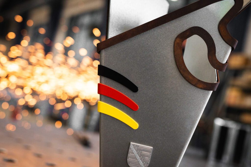 Nahaufnahme des deutschen MotoGP-Pokals mit den lackierten Nationalfarben Schwarz-Rot-Gold, dem sächsischen Wappen und dem geschwungenen Streckenlayout des Sachsenrings.