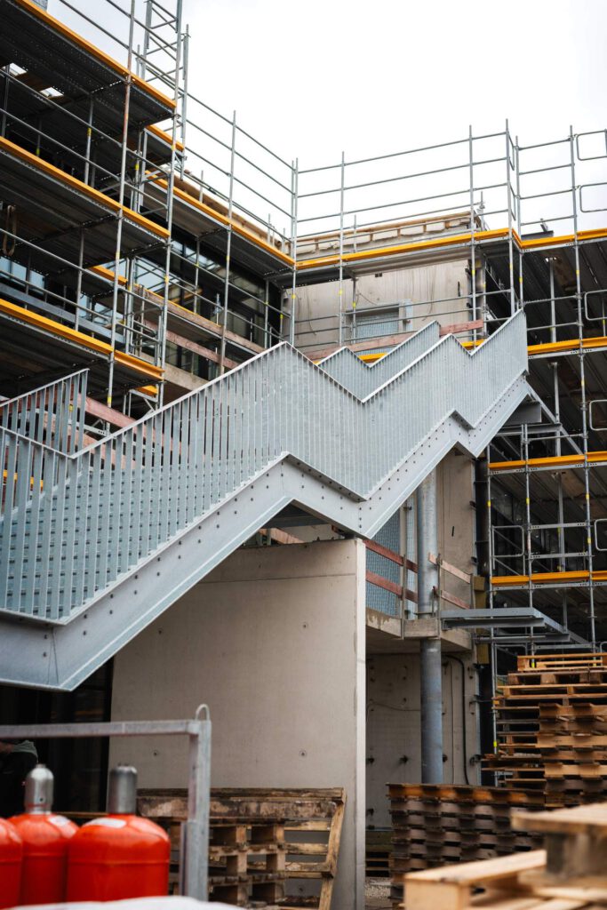 Komplett feuerverzinkte Fluchttreppe aus Stahl an einer Fassade in Haimhausen vor einem Baugerüst montiert.