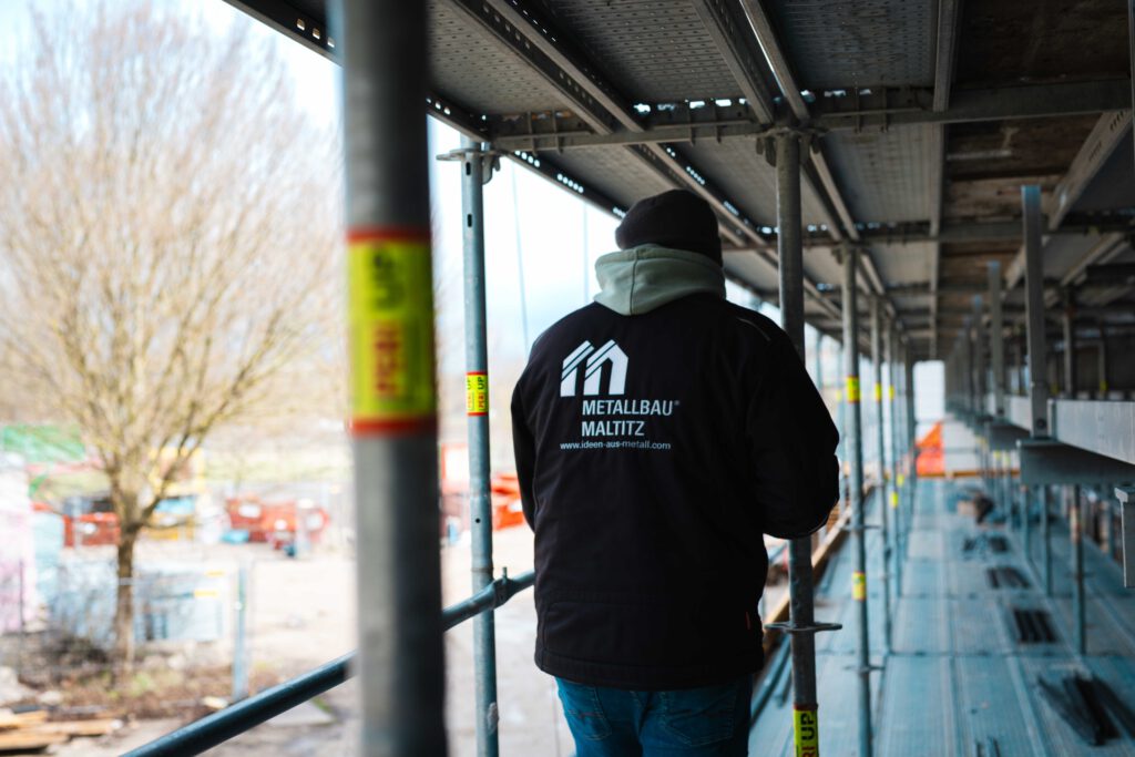 Rückansicht eines Metallbau Maltitz Mitarbeiters in Arbeitskleidung auf einem Baugerüst an einer Fassade.