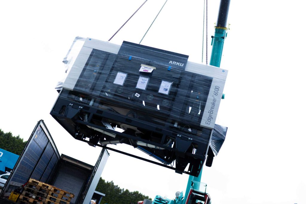 Die ARKU EdgeBreaker 6000 wird verpackt am Krangurt für den Transport zur Inbetriebsetzung angehoben.