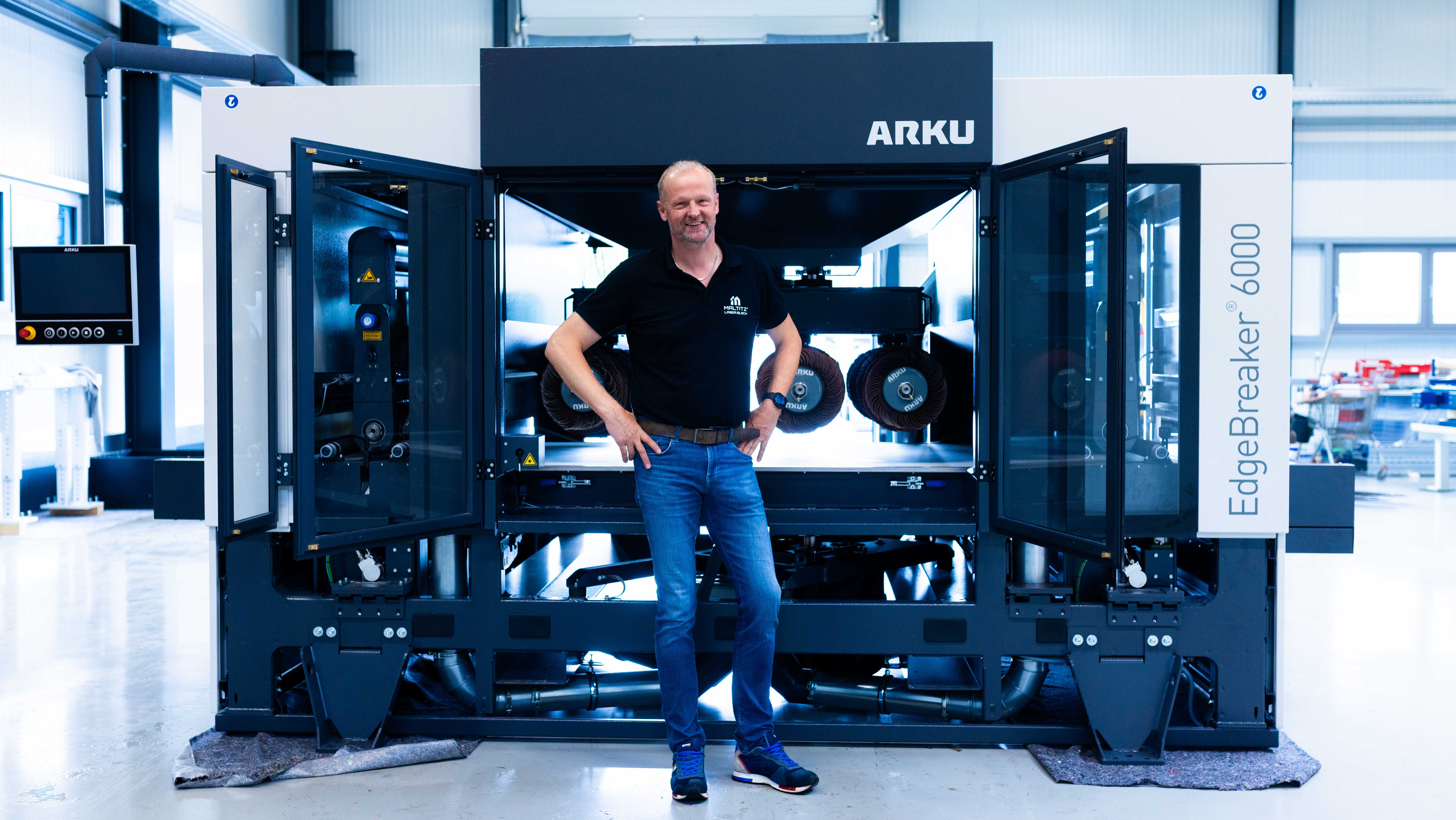 Geschäftsführer Dirk Maltitz steht lächelnd vor der geöffneten ARKU EdgeBreaker 6000 Entgratmaschine.