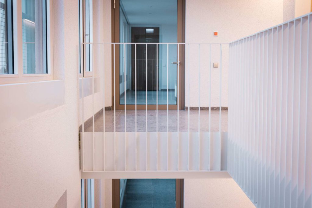 Maßgefertigte weiße Absturzsicherung und Metallgeländer im hellen Treppenhaus der Meiller Gärten in München