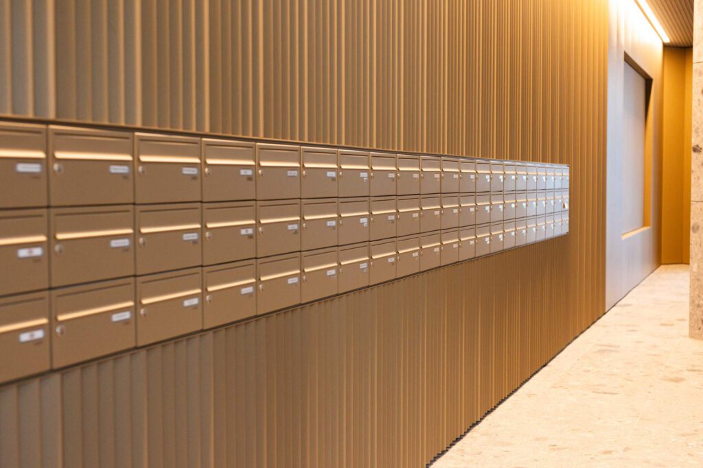 Lange Briefkastenanlage integriert in eine gefaltete Metallfassade im modernen Foyer der Meiller Gärten München